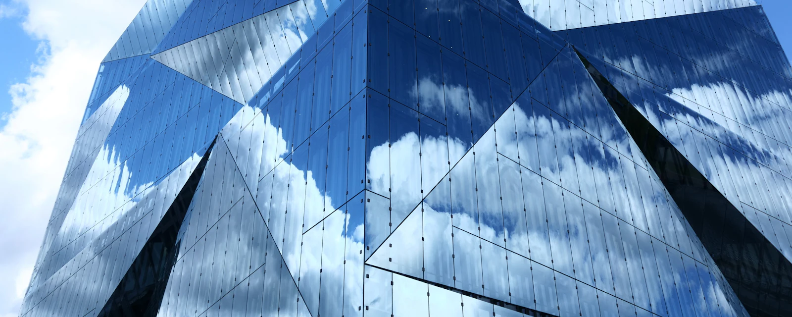 A faceted glass office tower reflecting blue sky and clouds